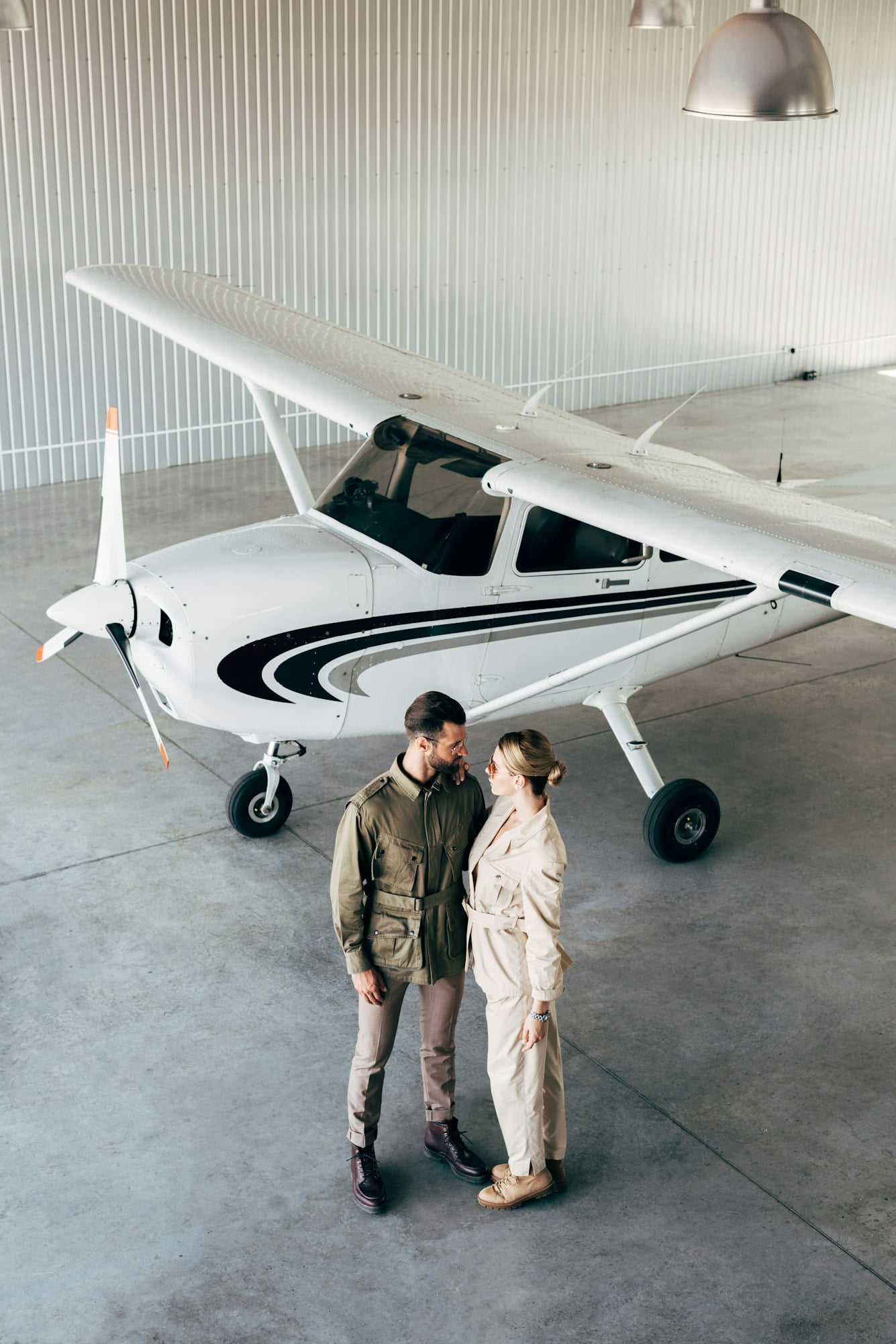 high angle view of couple in stylish jackets looking at each other in hangar with airplane